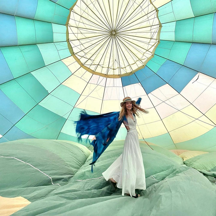 Pretty woman wearing boho-style clothes twirling inside a colorful, half-filled hot air balloon.