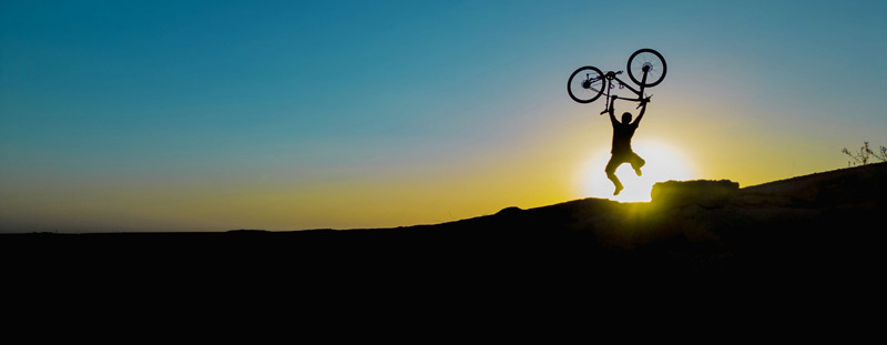 Silhouette of a person triumphantly holding a bicycle overhead at sunrise, symbolizing energy and vitality
