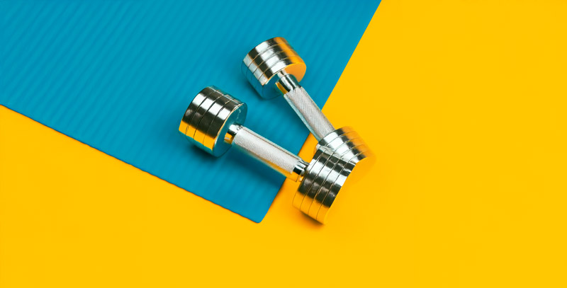 Metallic dumbbells on a blue mat, symbolizing strength and physical performance